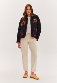 Čierna prešívaná bunda s ružovými detailmi, so súborom troch vyšitých rozprávkových postavičiek. Skombinovaná s krémovými nohavicami a žltými teniskami.