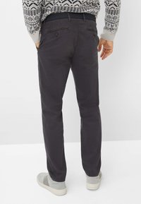 Chino grigio scuro con una texture liscia, dotati di tasche posteriori con chiusura a bottoni e abbinati a un maglione in maglia. Vestibilità e design casual.