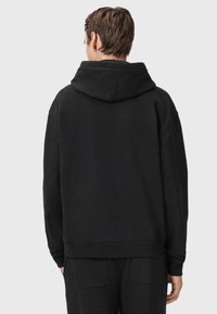 Czarna bluza z kapturem o luźnym kroju, z dużym kapturem, ściągaczami przy rękawach i na dolnym końcu, o miękkiej fakturze i minimalistycznym designie, noszona z dopasowanymi spodniami.