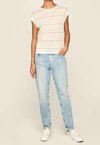 Kremowa bluzka z krótkim rękawem w poziome czerwone paski, zestawiona z jasnoniebieskimi dżinsami straight-leg i białymi sneakersami. Casualowy fason i prosty design.