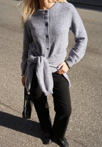 Gray knitted cardigan with buttons, belted at the waist; paired with black pants and black flat shoes. Subtle texture, casual fit.