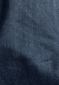 Tmavě modrý denim s hladkou texturou, který má lehký lesk a jemné bílé švy. Tkaní je pevné a rovnoměrné.