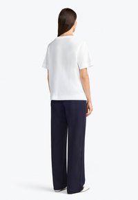 Haut blanc à manches courtes avec une coupe décontractée, associé à un pantalon large bleu marine. Tissu lisse, design simple et silhouette droite.