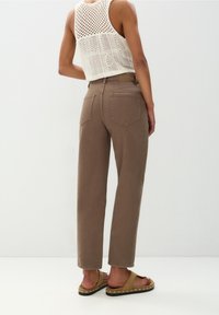 Jean marron taille haute avec une coupe décontractée et des poches arrière, associé à un débardeur en maille blanc et des sandales slides couleur sable.