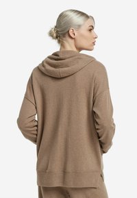 Brązowa bluza z kapturem o luźnym kroju, z prążkowanym wykończeniem na dole i miękką fakturą. Posiada podwójną warstwę kaptura i obniżone ramiona dla wygody.