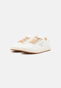 Weiße Sneakers aus strukturiertem Material, mit beigen Schnürsenkeln und einer braunen Gummisohle. Verfügt über gestickten Text und ein lederähnliches Detail an der Ferse.