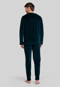 Conjunto de pijama de forro polar verde oscuro, que incluye una parte superior de manga larga y pantalones a juego. Textura suave, corte relajado, con un diseño simple y sin patrones visibles.