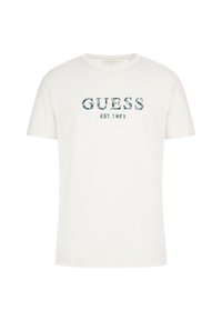 T-shirt en coton blanc avec un logo "GUESS" à motifs bleu-vert et le texte "EST. 1981". Manches courtes et col ras du cou.