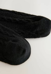 Calcetines negros de punto con puños acanalados, con un patrón texturizado y punteras redondeadas, que muestran una apariencia suave y peluda.