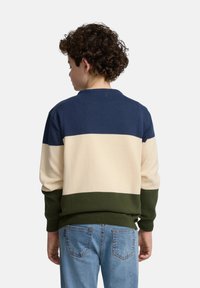 Sudadera de punto con rayas horizontales en azul marino, crema y verde oliva, puños y dobladillo acanalados. Combinada con jeans de mezclilla de color azul claro.