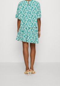 Vestido de estampado floral con un corte holgado, mangas cortas y falda con volantes. Presenta un detalle de escote en forma de lágrima en la parte posterior. Los colores incluyen verde, rosa y blanco.