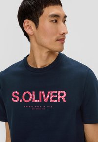 Navyblauwe katoenen t-shirt met een prominent roze patroon van het "S.OLIVER" logo en tekst, korte mouwen en een ronde hals.
