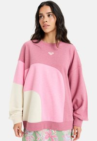 Sweatshirt i pink og creme, med farveblokdesign og rund form. Fremstillet af blødt stof, med et lille logo på brystet.