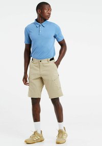 Lichtblauw polo shirt met korte mouwen, beige cargo shorts met zijritszak, en beige sportschoenen met witte sokken.