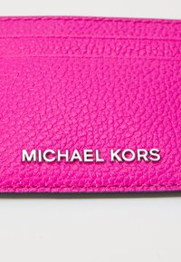 Różowy skórzany portfel na karty o fakturze z srebrnym logo "MICHAEL KORS". Posiada przegródki na karty oraz smukły design.