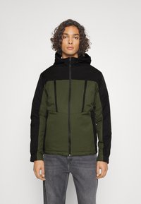 Kapućasta jakna s zelenim dijelom i crnim detaljima, s džepovima na patentni zatvarač i glatkom teksturom. Slim fit dizajn s modernim sportskim oblikom.