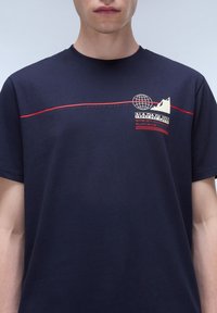 Camiseta de manga corta color azul marino hecha de algodón, con un gráfico de un globo terráqueo y una montaña en crema y rojo, acompañado de texto descriptivo.