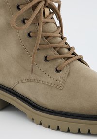 Bottines en daim taupe avec bout rond, lacets beige et œillets noirs. Semelle épaisse moulée avec texture pour une meilleure adhérence.