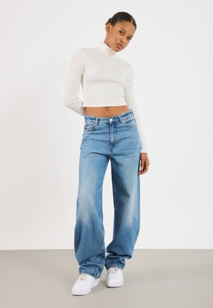 Valge ribaga turtleneck crop top koos helesiniste laiade denimpükstega, täiendatud valgete tossudega. Lihtne disain, pehme tekstuur.