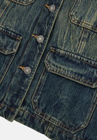 Giacca in denim di colore blu scuro con un finish sbiadito. Caratterizzata da bottoni a pressione argentati, due tasche frontali e cuciture gialle a contrasto.