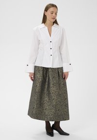 Balta krekla ar garām piedurknēm un ar pogām, apvienota ar ceļgalu garuma zelta un melnā rakstainu svārku. Melni papēži pabeidz apģērbu.