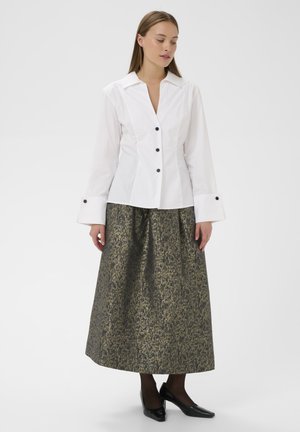 Weißes, langärmeliges Hemd, kombiniert mit einem knielangen Rock im gold-schwarzen Muster. Schwarze High Heels runden das Outfit ab.