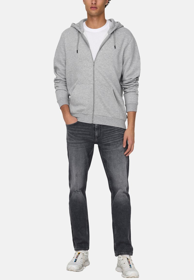 Gray zip-up hoodie in soft fabric with drawstrings, paired with dark gray jeans and white sneakers. Features pockets and a relaxed fit.