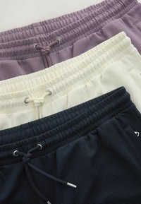 Trois tailles avec cordon texturées de shorts en violet clair, écru et noir, superposées sur un fond clair.
