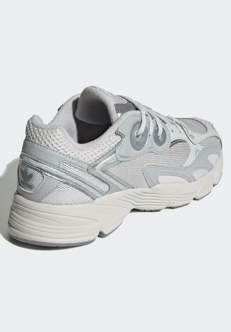 Zapatilla deportiva gris con superposiciones de malla y sintéticas, acentos texturizados, cuello acolchado y una suela de goma gruesa. Los cordones se extienden sobre la lengüeta.