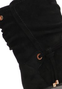 Botín de ante negro hasta el tobillo con un diseño arrugado, que cuenta con un cierre de cordones y ojales en tono cobre. Textura suave con detalles de costura decorativa.