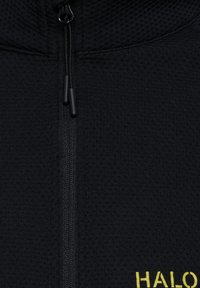 Schwarze, gewobene Jacke mit Reißverschluss, der aus strukturiertem Stoff gefertigt ist. Sie hat einen glatten Reißverschluss und ein gelbes "HALO"-Label nahe dem Saum.