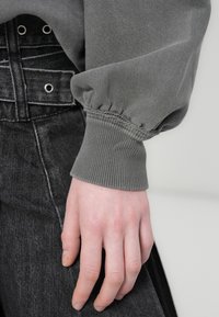 Γκρι φούτερ με σφιχτά μανίκια, ριμπ τελείωμα και μαλακή υφή, συνδυασμένο με μαύρο τζιν ψηλόμεσο με μεταλλικές λεπτομέρειες.
