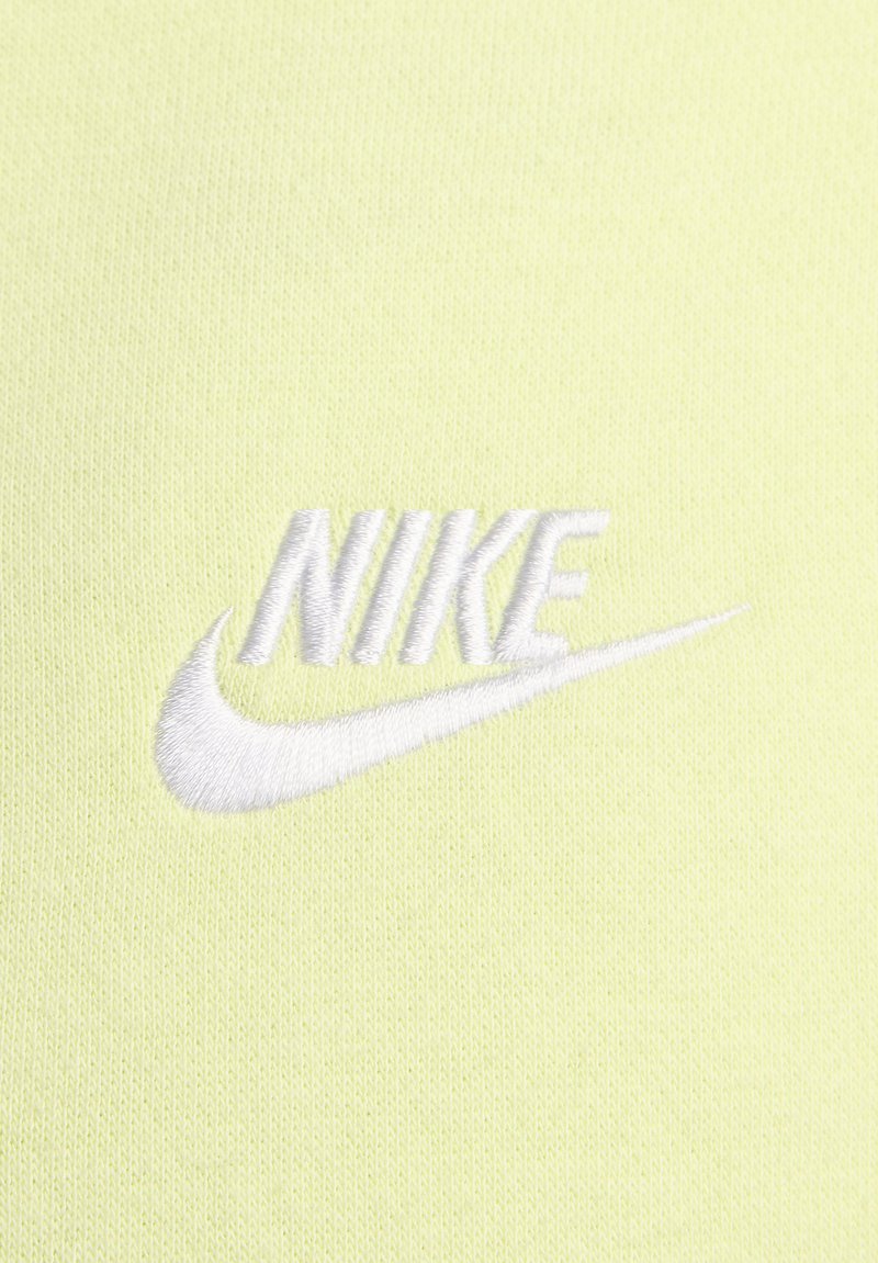 Tessuto giallo chiaro con una finitura testurizzata, decorato con un ricamo bianco del logo "NIKE" e un design a swoosh.