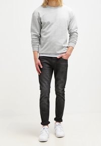 Grå sweatshirt med långa ärmar, kombinerad med mörka jeans, med en slim fit och uppvikta ärmslut. Bärs med vita sneakers.