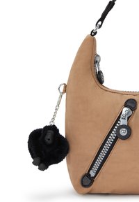 Vaaleanruskea olkalaukku, jossa on sileä synteettinen materiaali, musta vetoketju, mustat metalliosat ja irrotettava pörröinen musta apina avaimenperä.