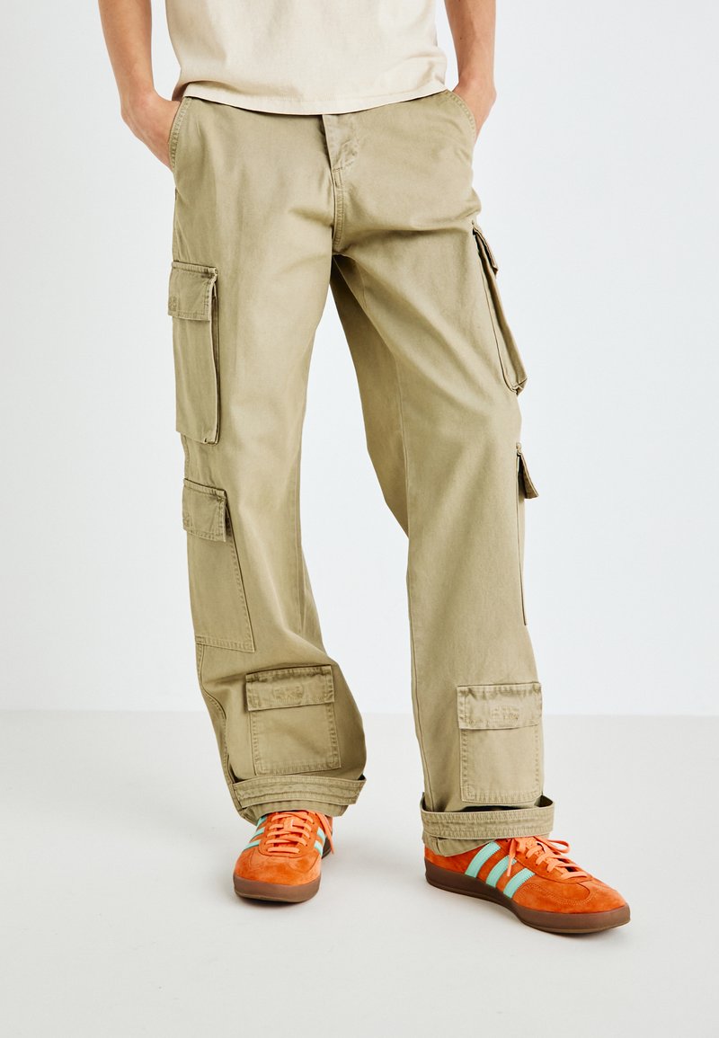 Khakifarbene Cargo-Hose mit mehreren Seitentaschen, geradem Schnitt und weicher Textur, kombiniert mit orangefarbenen Sneakers mit blauen Streifen.