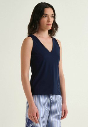 Donna con capelli scuri fino alle spalle indossa un top senza maniche blu navy a scollo a V e pantaloni a righe blu e bianche con stampa floreale.