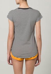 Camiseta de rayas en blanco y negro con mangas cortas, escote redondo y dobladillo curvado. Combinada con pantalones cortos de tiro naranja en la cintura.