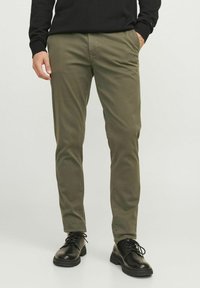Chinos verde oliva con corte ajustado, fabricados en una mezcla de algodón, con bolsillos delanteros y combinados con zapatos negros de lace-up.