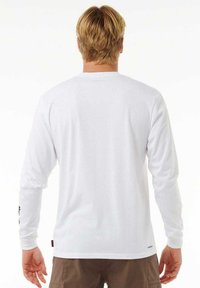 Camisa blanca de mangas largas, hecha de una tela suave, con un escote redondo y una pequeña etiqueta en el lado inferior. Sin patrones ni adornos visibles.