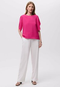 Top corto de fucsia con un acabado texturizado, combinado con pantalones anchos blancos y sandalias de tacón negro. Silueta elegante y moderna.