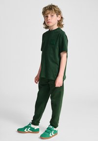 Mørkebrun bomulds T-shirt med lomme og matchende sweatpants. Grønne sneakers med hvide detaljer. Enkel, afslappet pasform og struktur.