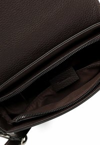 Sac à main en cuir marron avec surface texturée. L'intérieur présente un revêtement en tissu foncé et un compartiment zippé. Design simple et fonctionnel.