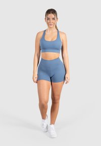 Lichtblauwe sport-bh en bijpassende hoge shorts, gemaakt van een zachte stof met een gladde textuur. Witte sportschoenen maken de outfit compleet.