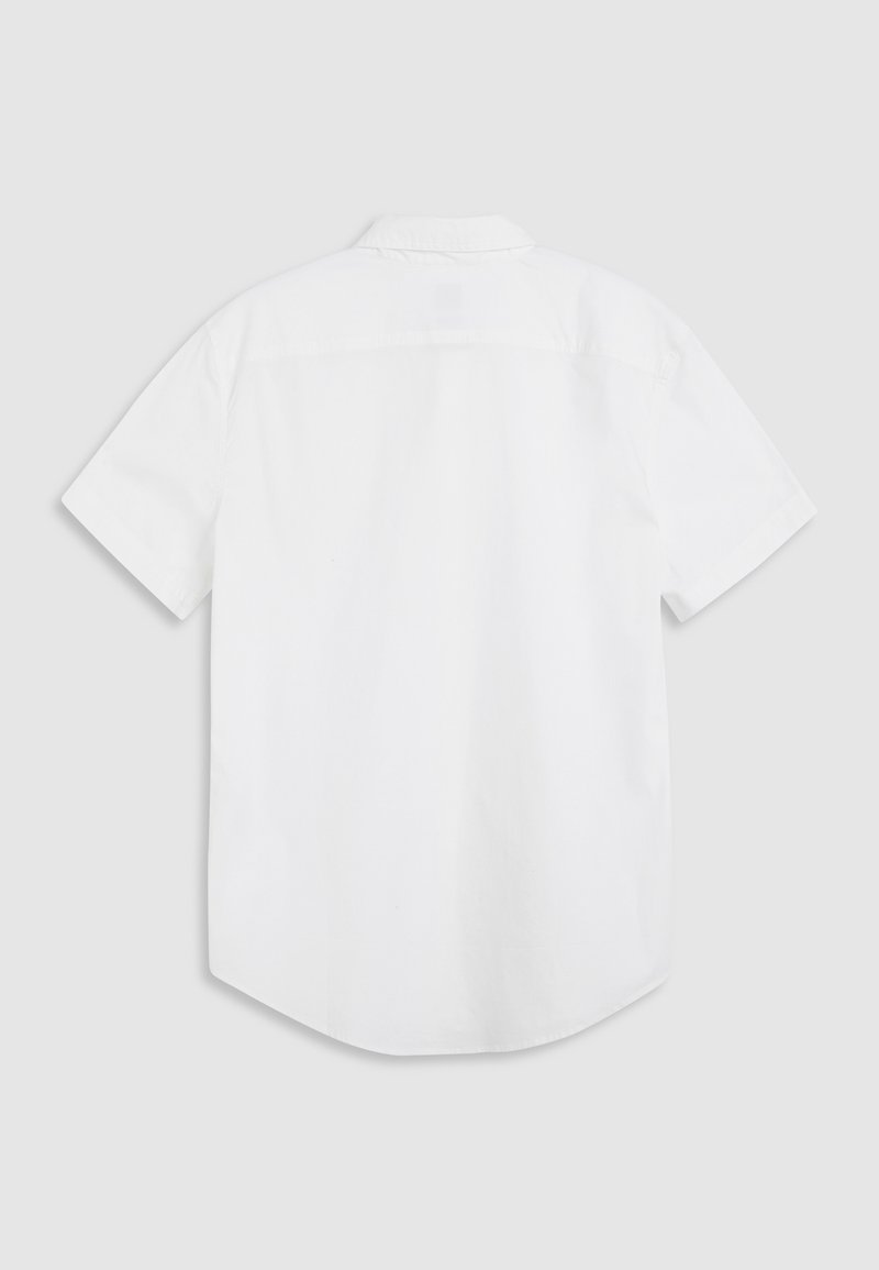 Chemise blanche à manches courtes en coton. Elle présente un col boutonné et un ourlet arrondi, avec une texture lisse et sans motifs.