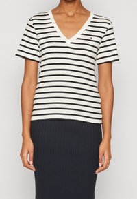 T-shirt bianco a V con righe orizzontali nere, maniche corte e un piccolo logo sul lato sinistro del petto, realizzato in morbido cotone.