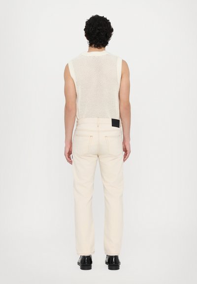 Top tricotat fără mâneci, de culoare crem, cu un model texturat; asortat cu blugi drept crem și pantofi negri. Design minimalist.