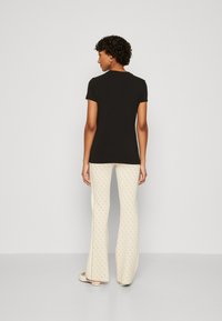 Camiseta negra de manga corta combinada con pantalones de campana de color claro y con estampado. El atuendo tiene un corte relajado y detalles de diseño simples.