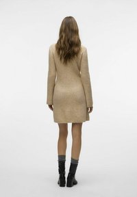Robe tricotée beige côtelée à manches longues, longueur genou, avec une silhouette ajustée et un ourlet brut. Associée à des bottes noires jusqu'au genou.