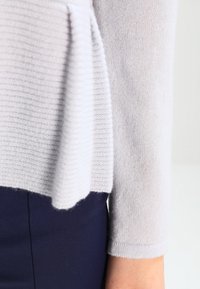 Lichtgrijze trui met een textuur ribbels patroon aan de zoom en gladde mouwen, aangevuld met een donkerblauwe onderkleding.